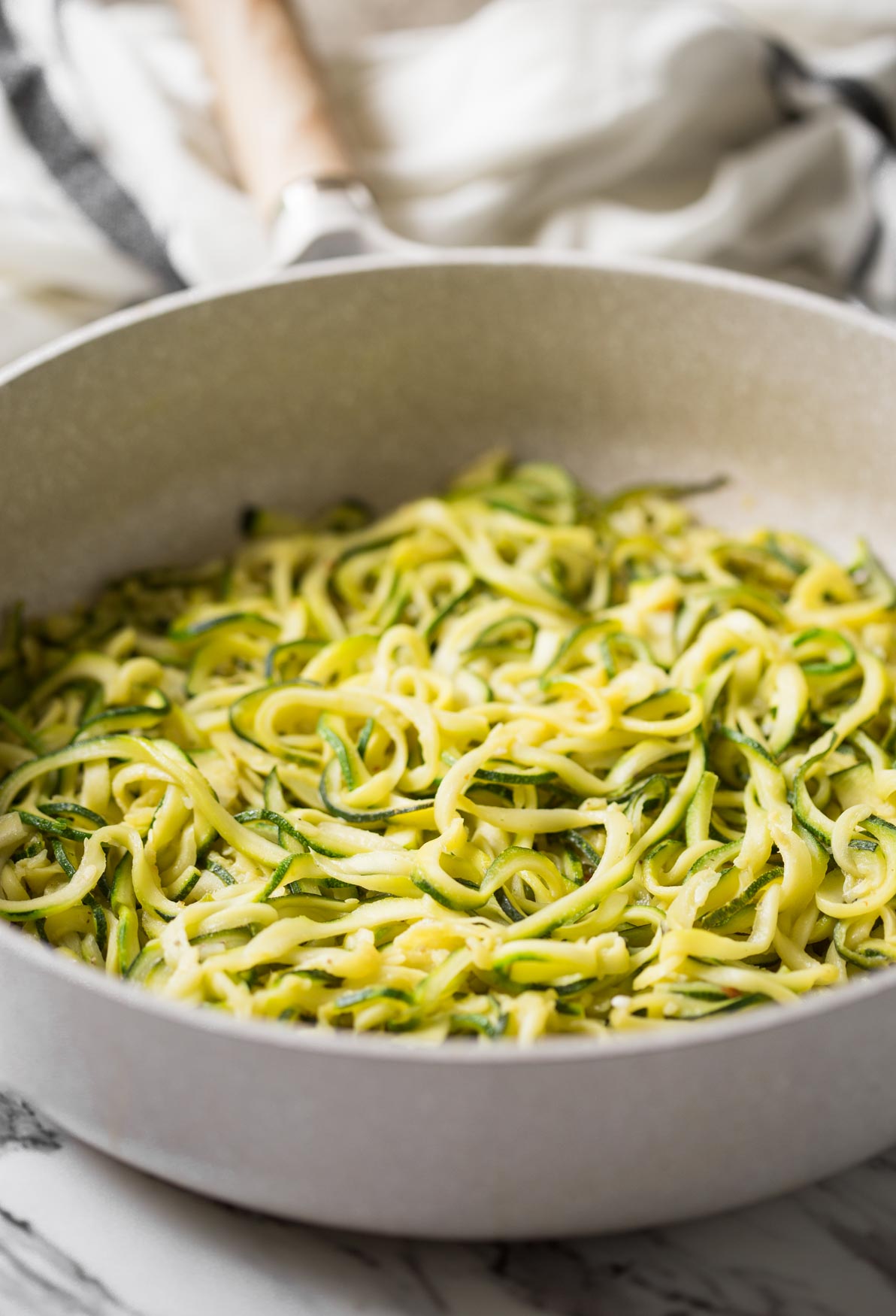 Fresh zucchini noodles stir-fried in a skillet with chili, garlic, and olive oil.