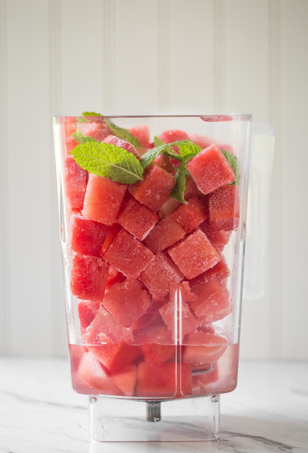 Frozen watermelon cubes with fresh mint and water in a blender jar