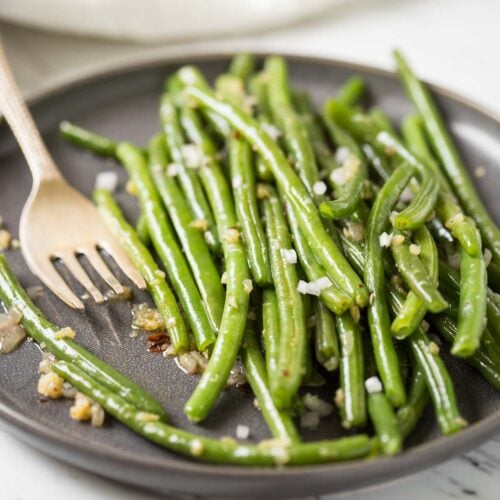 Sauteed garlic green beans in a serving plate with spoon