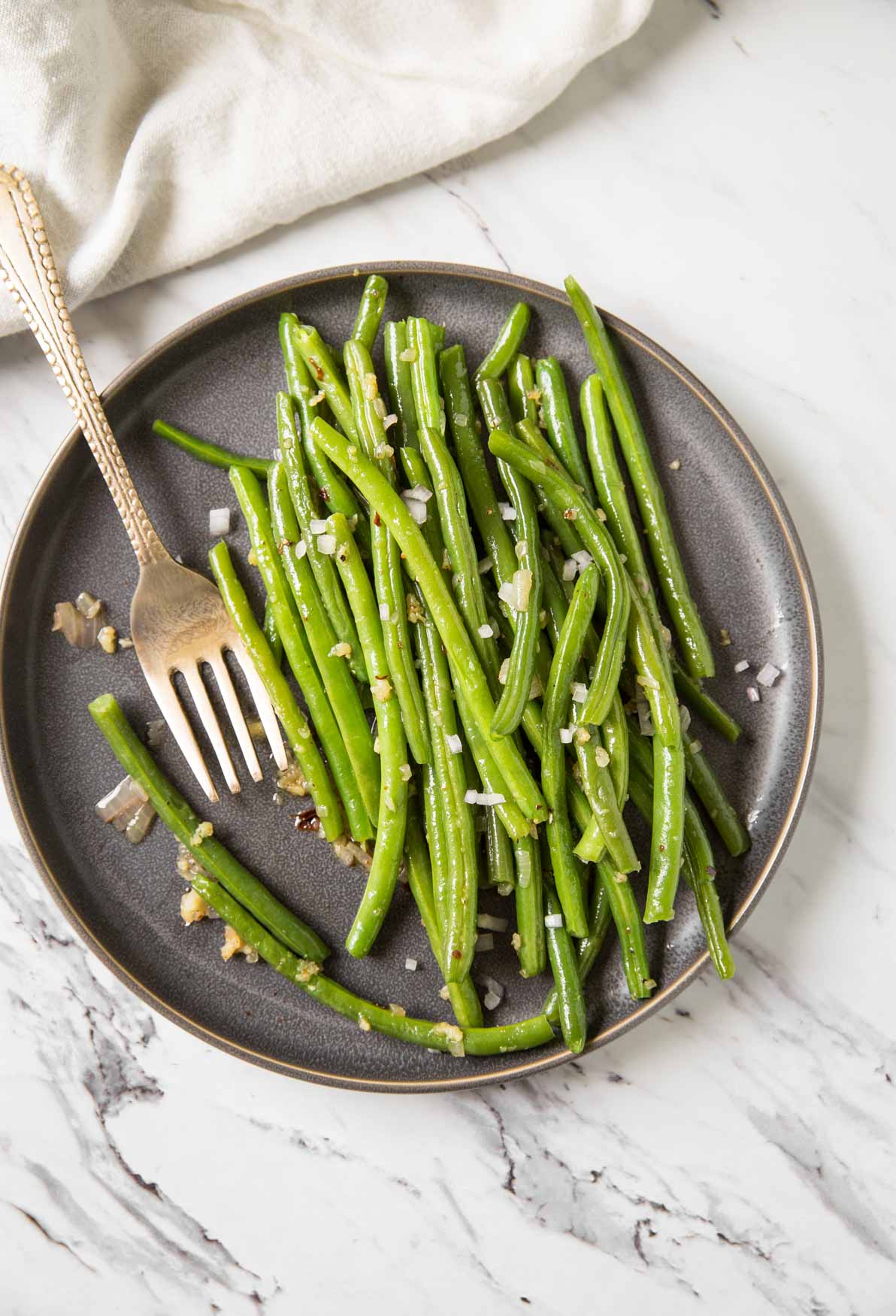 Sautéed garlic green beans in a serving plate with spoon.