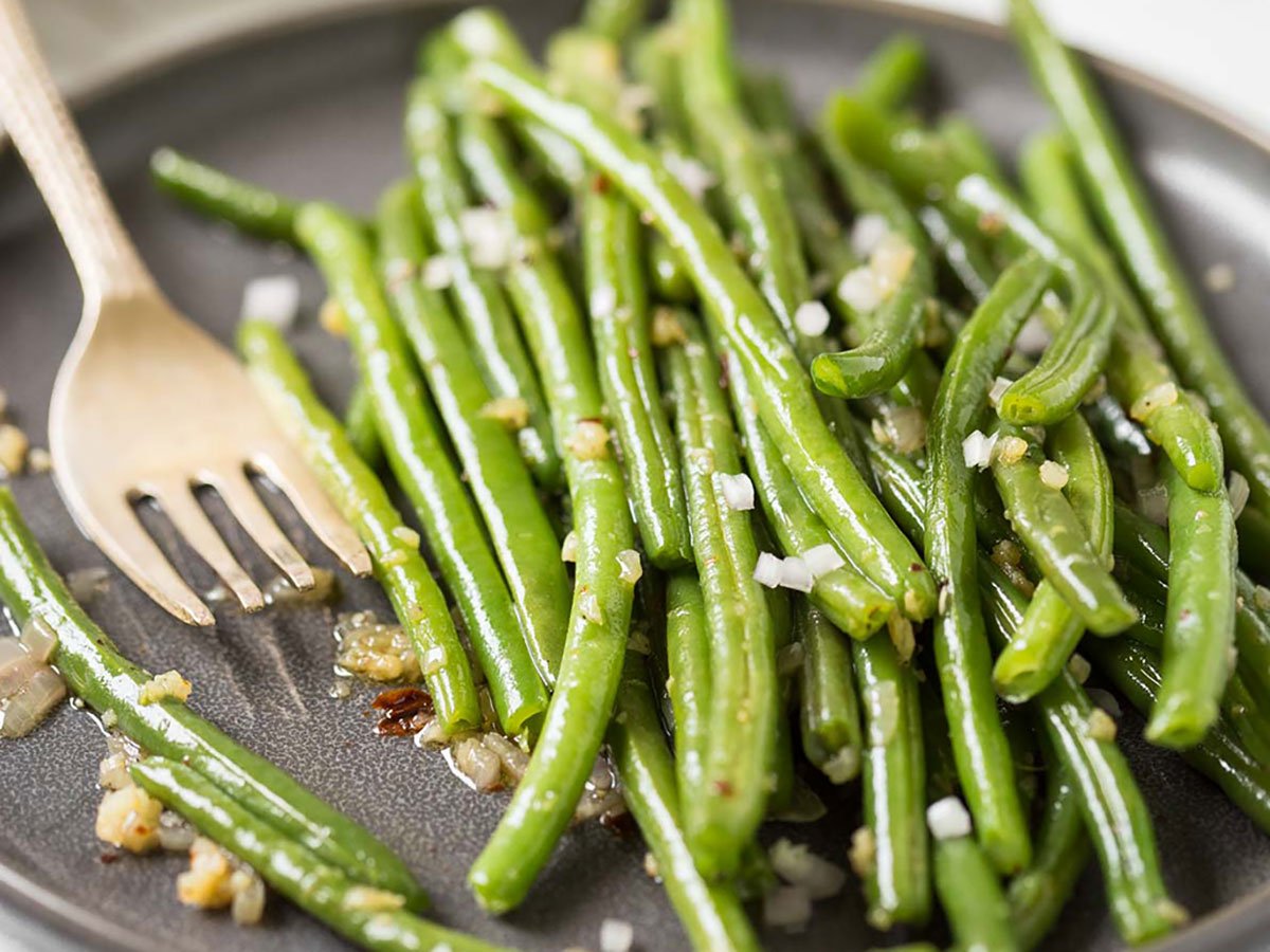 Sautéed garlic green beans in a serving plate with spoon.