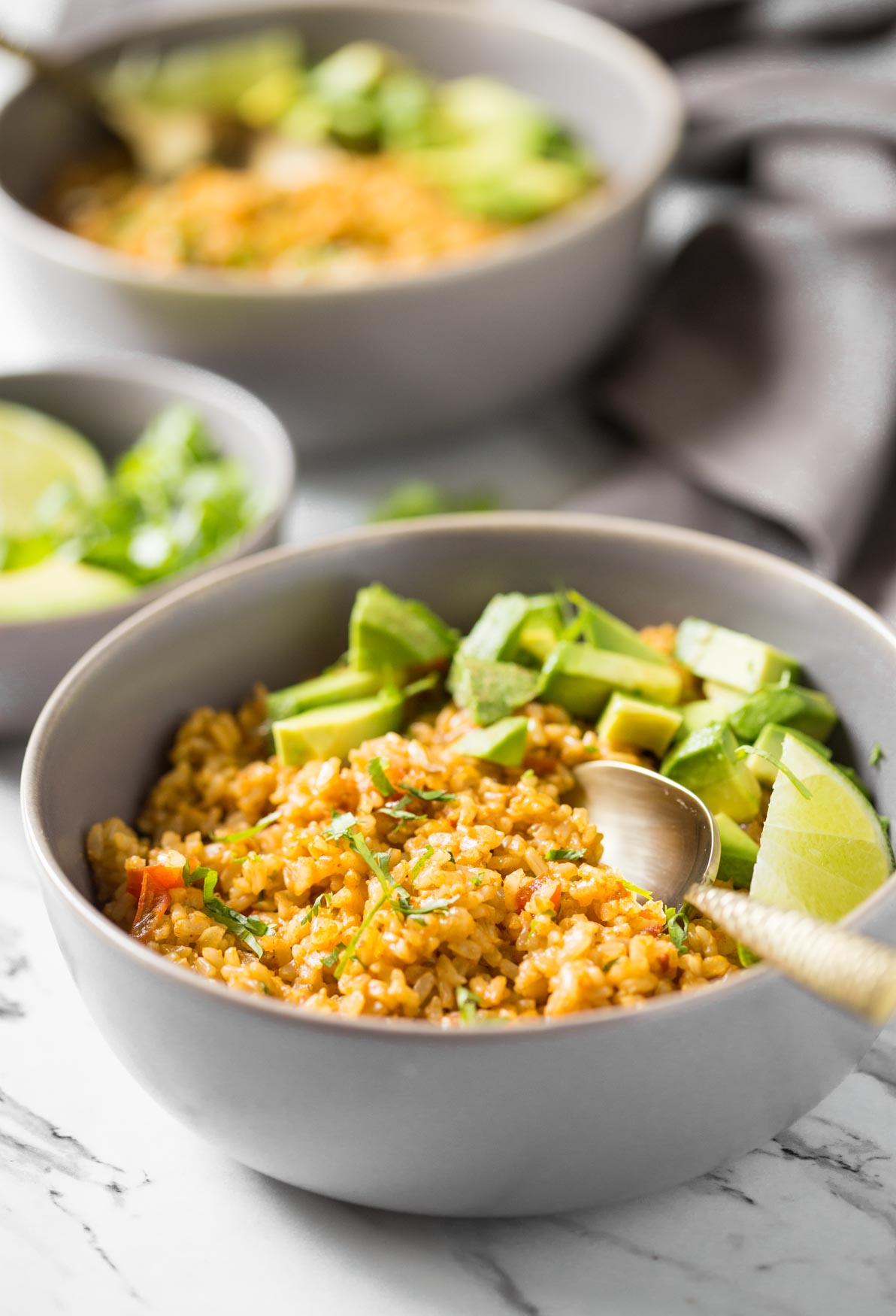 Mexican brown rice in a bowl with avocados, lime, and a spoon