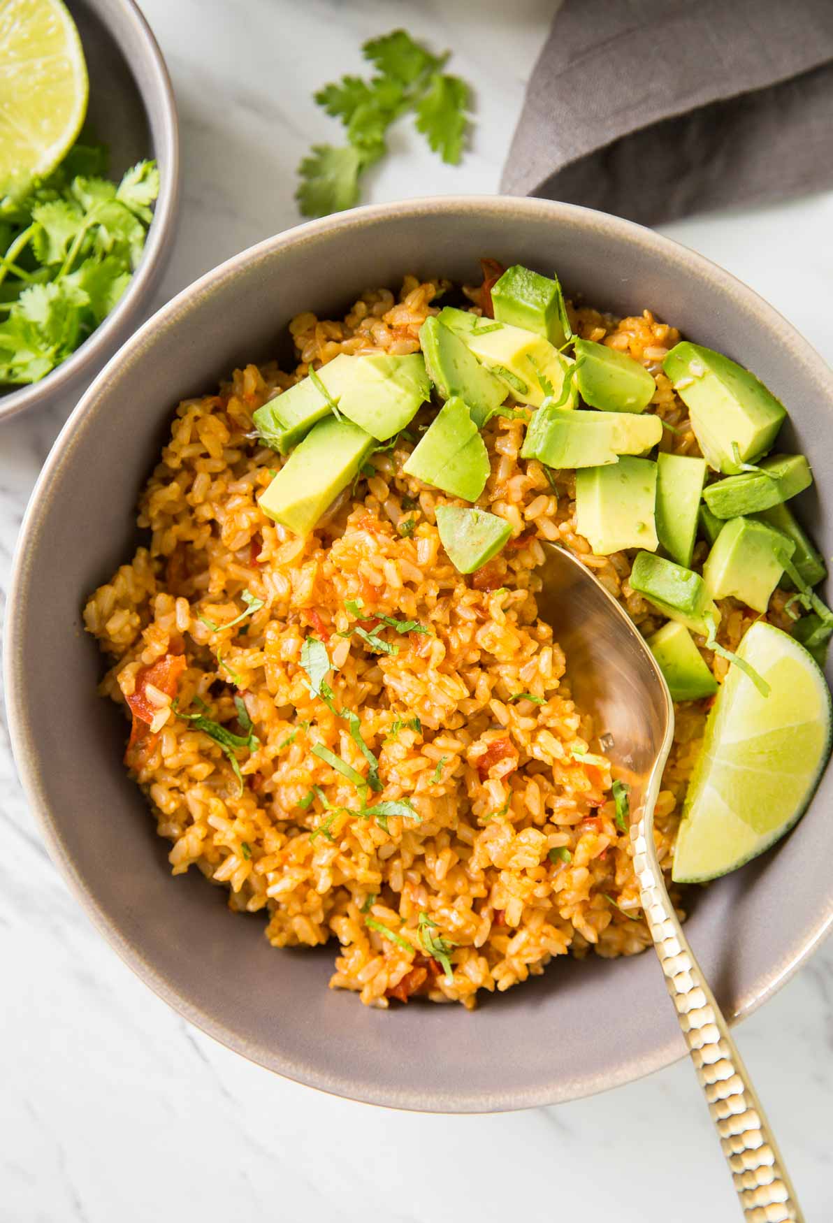 Mexican brown rice in a bowl with avocados, lime, and a spoon
