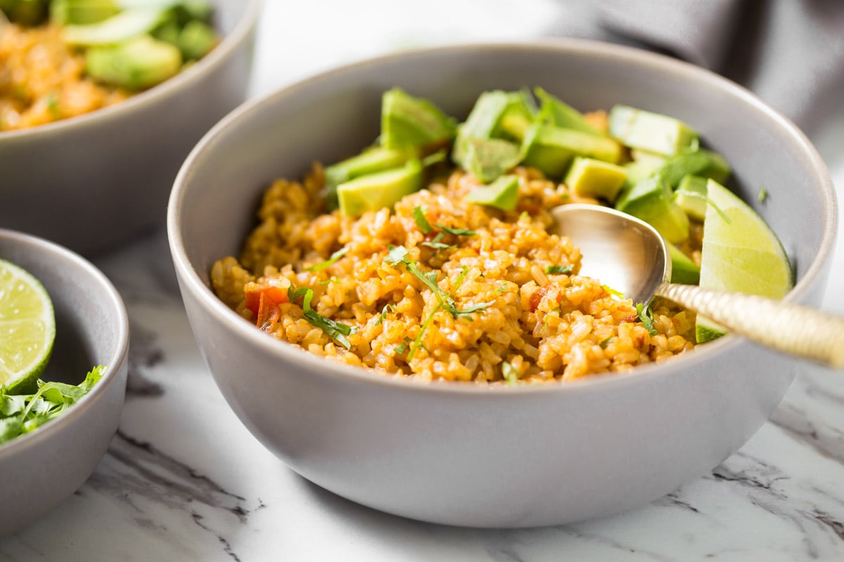 Mexican rice in a bowl with avocados, lime, and a spoon