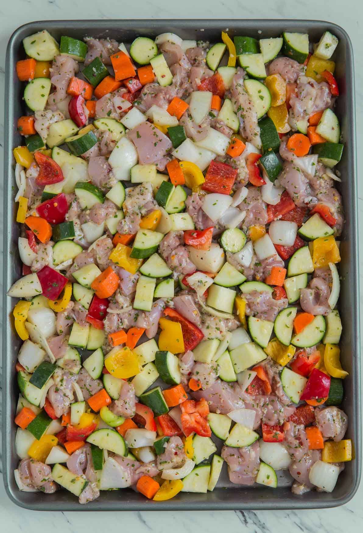 Marinated chicken and vegetables in a baking tray ready to go in the oven