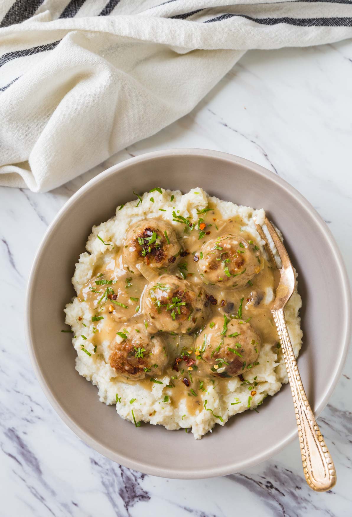 Healthy ground turkey meatballs with gravy and mashed cauliflower in a serving deep dish