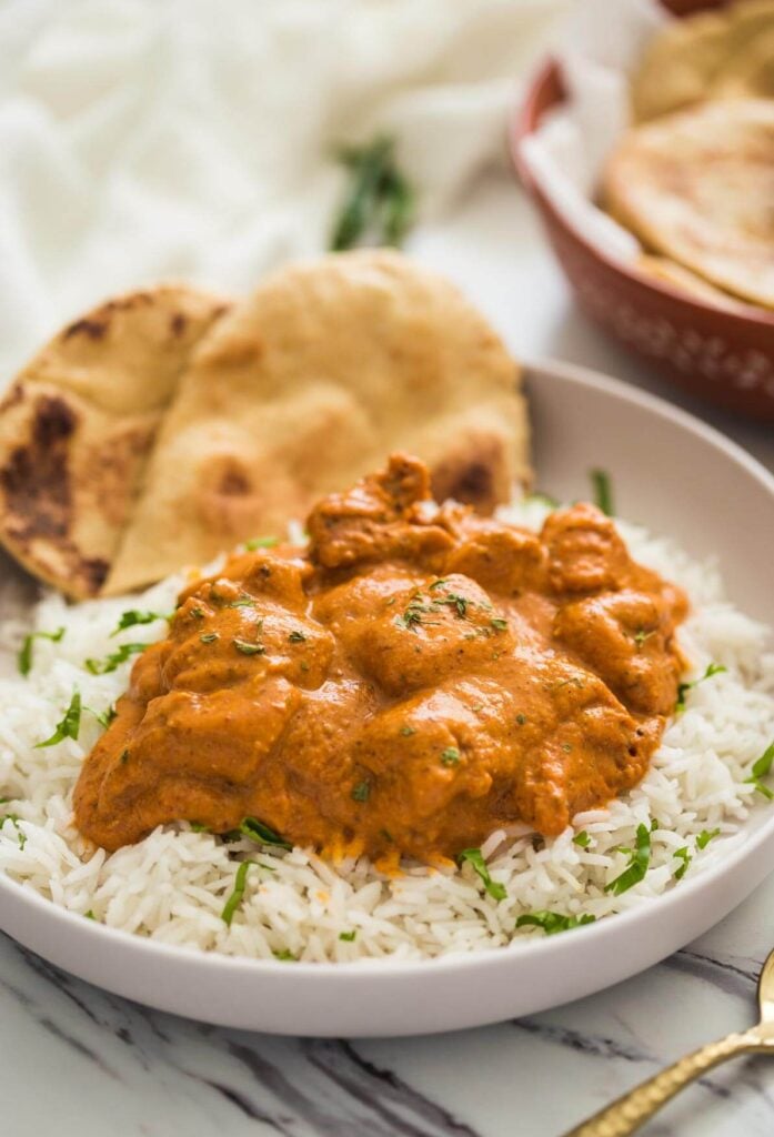 Restaurant style chicken tikka masala ready to serve in serving plate with homemade naan bread and plain rice