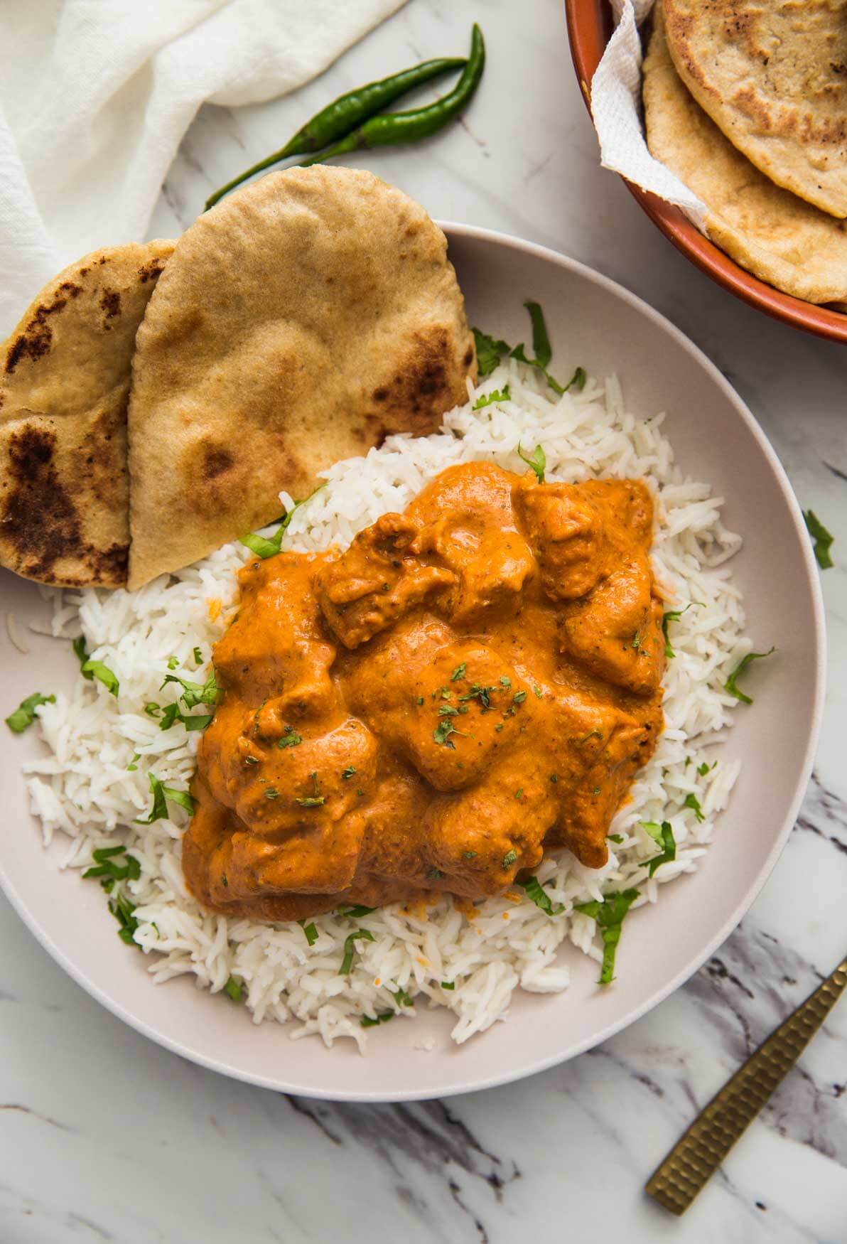 Restaurant style chicken tikka masala ready to serve in serving plate with homemade naan bread and plain rice