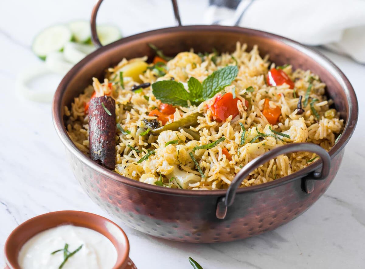 Indian vegetable biryani in a serving bowl and raita on the side