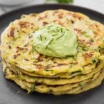 Healthy zucchini pancakes stacked in a serving plate with a dollop of green avocado sauce