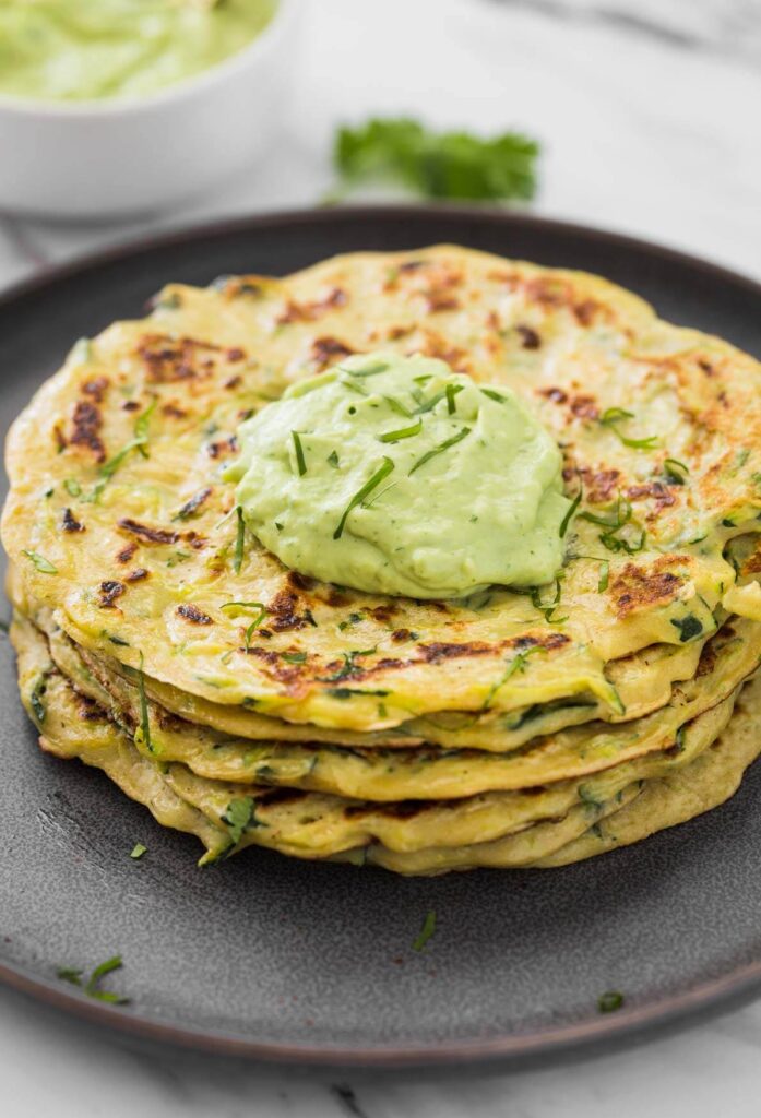 Healthy zucchini pancakes stacked in a serving plate with a dollop of green avocado sauce