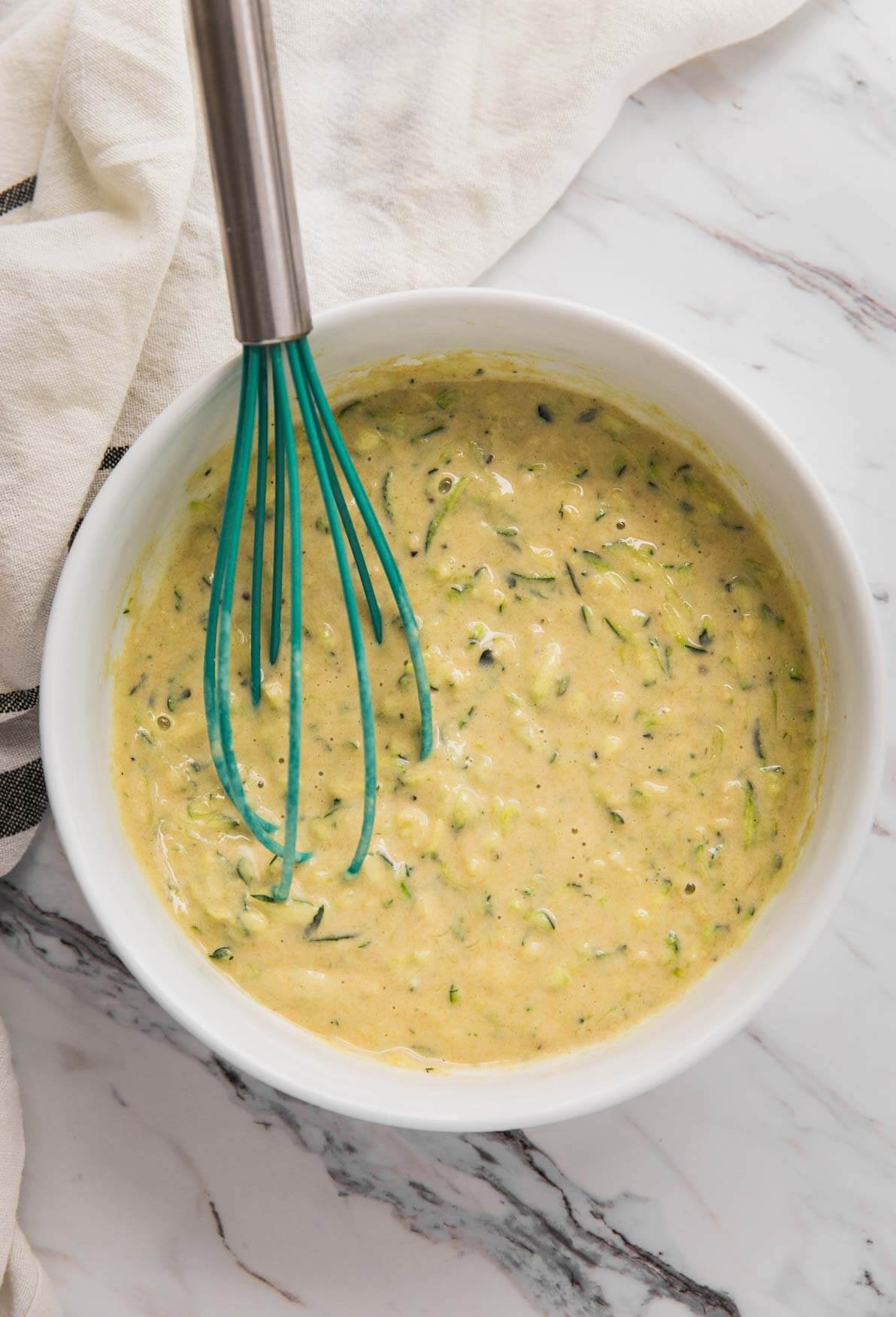 grated zucchini and flour batter in a mixing bowl with a whisk