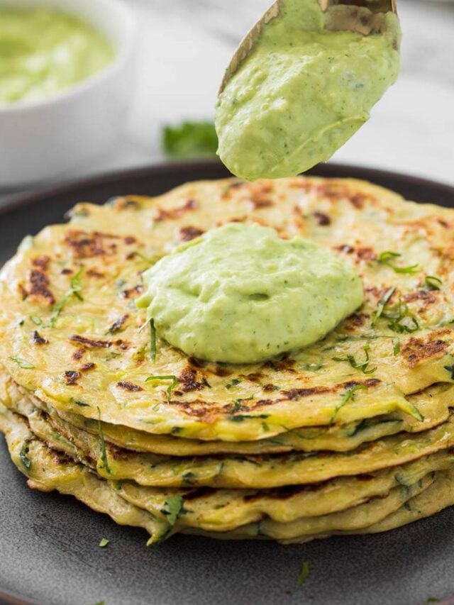 Healthy zucchini pancakes stacked in a serving plate with a dollop of green avocado sauce.
