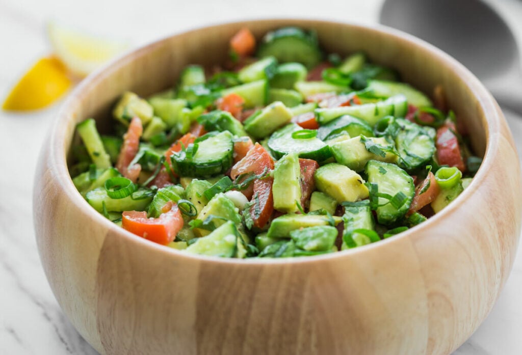 photo of avocado cucumber salad with tomato in a large wooden bowl