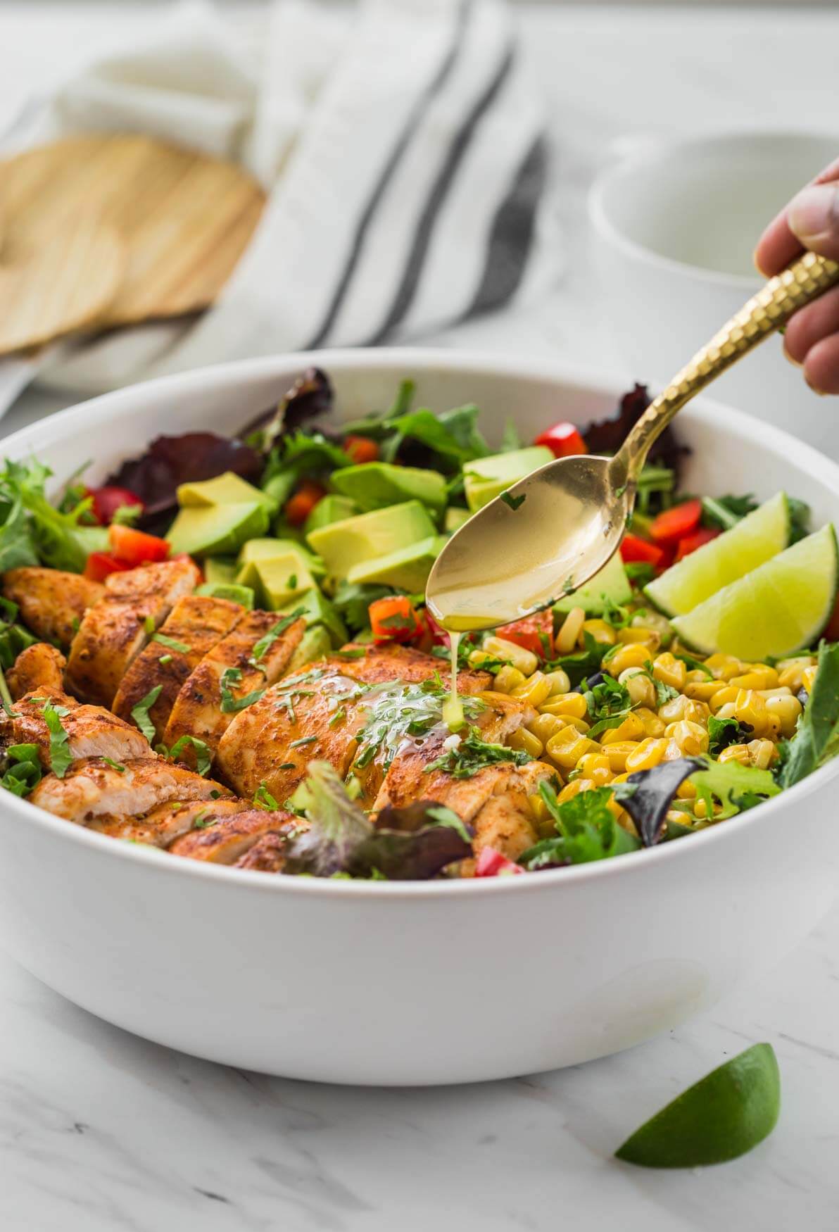 drizzling cilantro lime dressing oven Mexican Chicken Avocado Salad in a salad bowl.