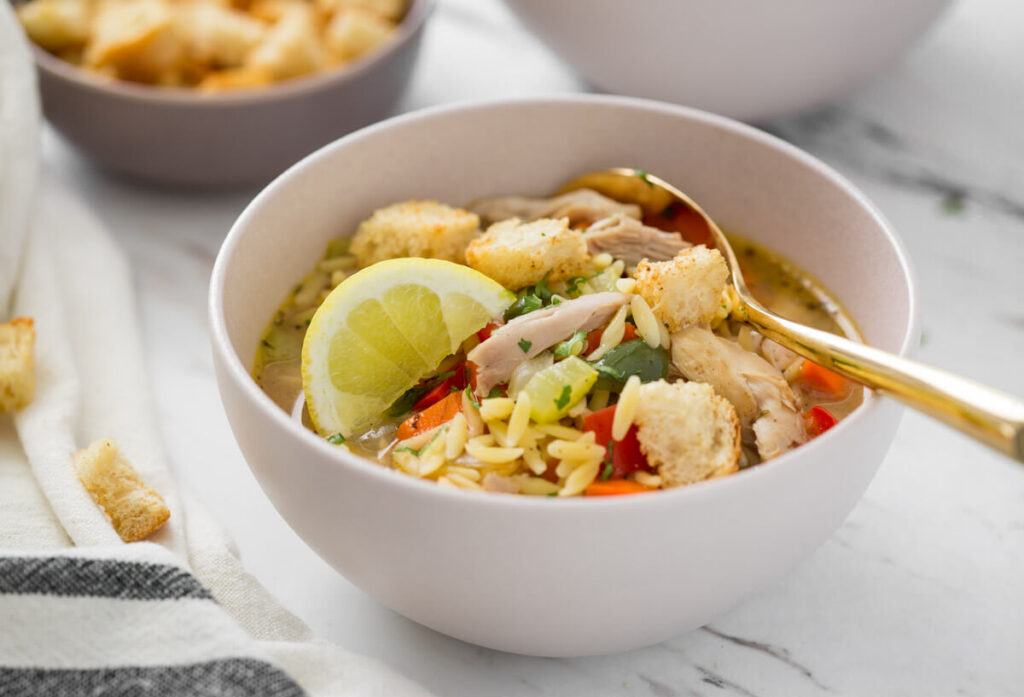 lemon chicken orzo soup in a serving bowl with some croutons on the side.