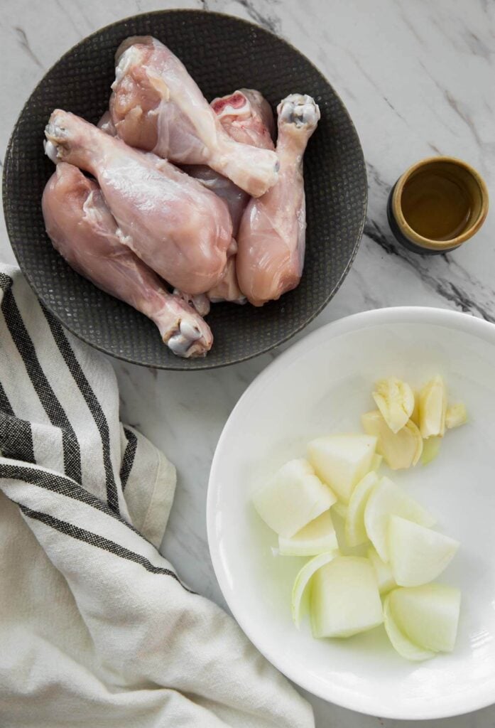image of chicken drumsticks in a bowl and diced onion and garlic in in a plate