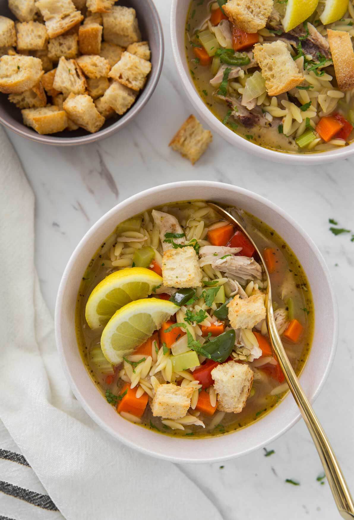 Healthy lemon chicken soup with orzo in a serving bowl with some croutons on the side.