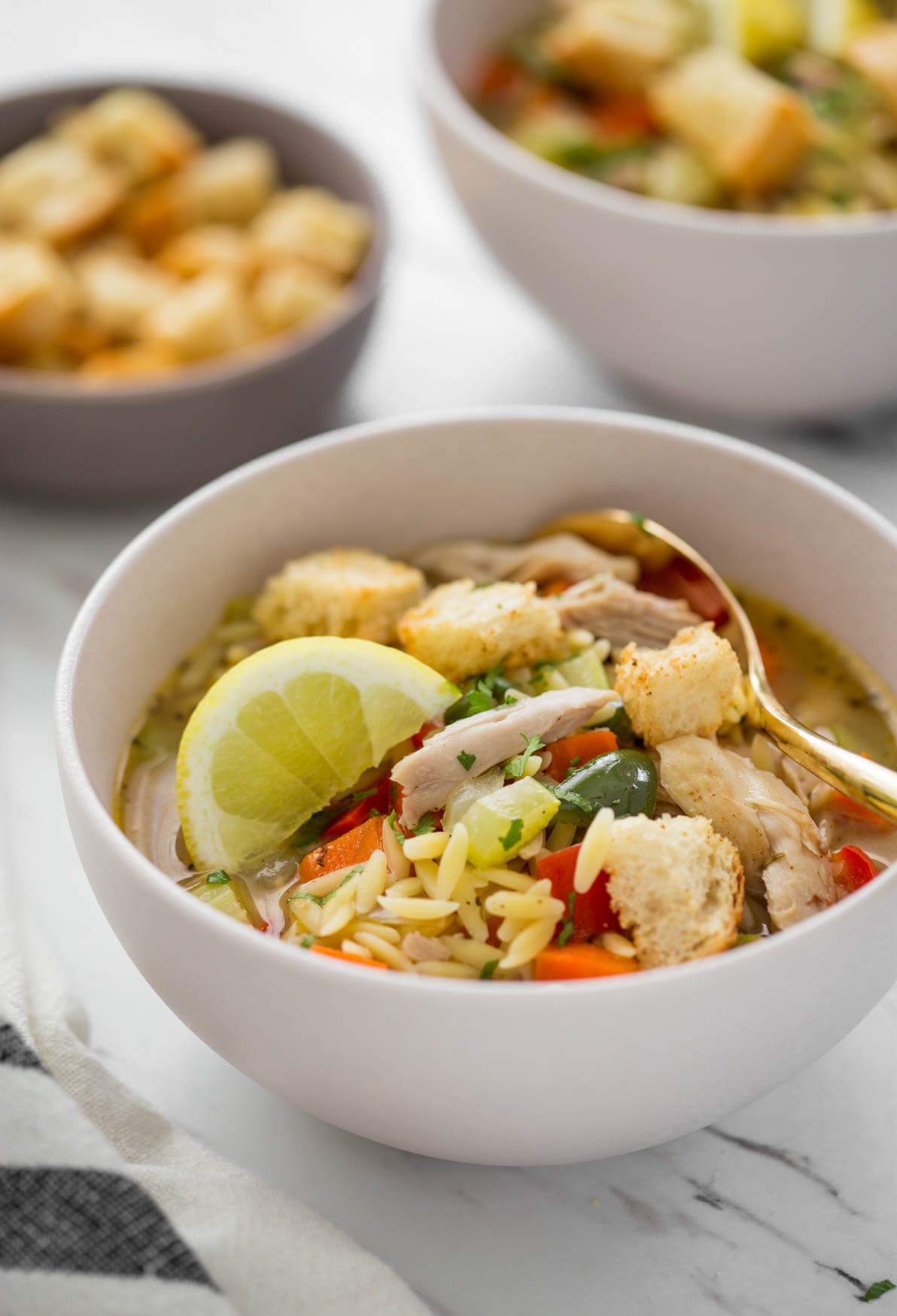 Healthy lemon chicken soup with orzo in a serving bowl with some croutons on the side.