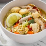 lemon chicken orzo soup in a serving bowl with some croutons on the side.