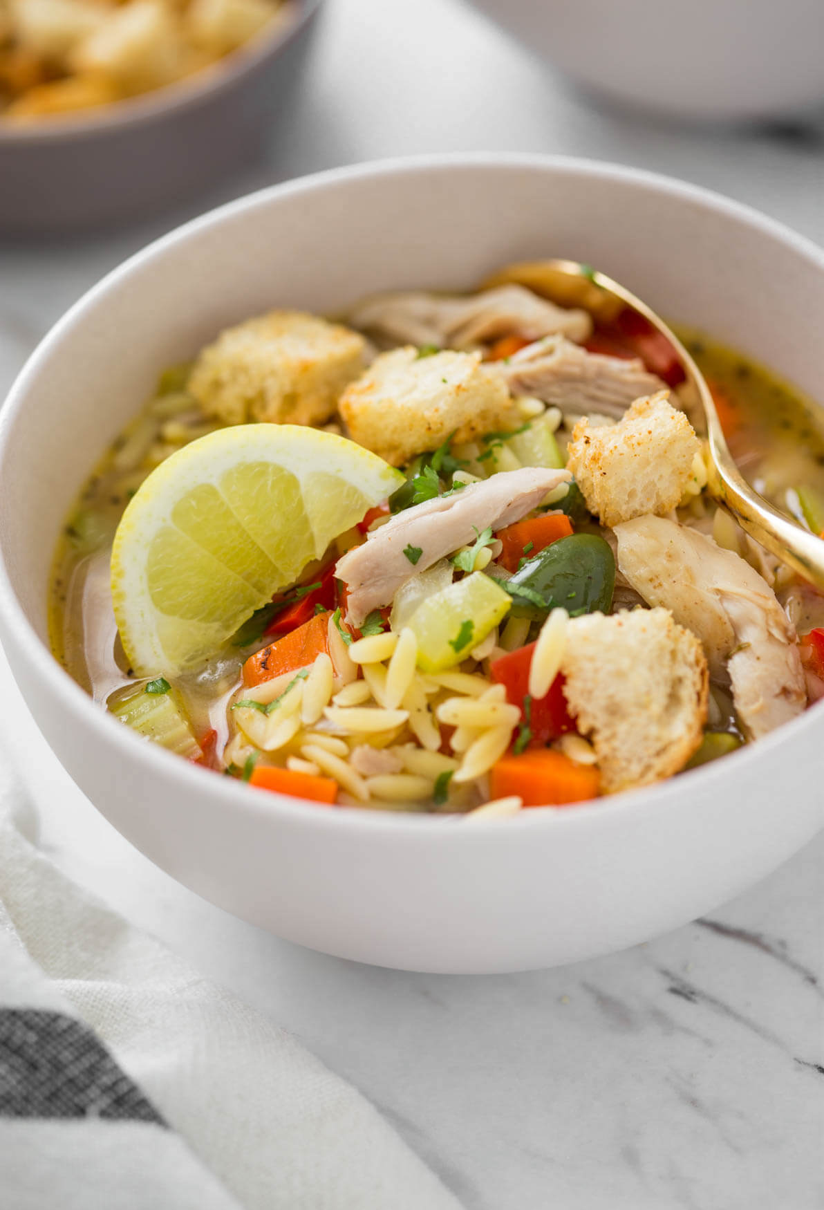 lemon chicken orzo soup in a serving bowl with some croutons on the side.