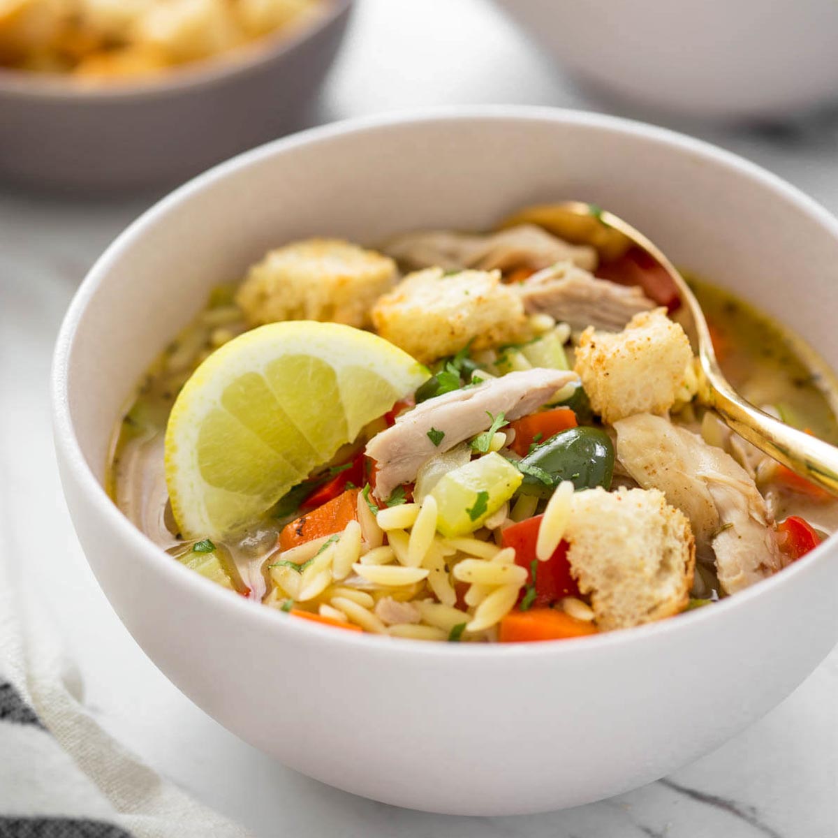 Healthy lemon chicken soup with orzo in a serving bowl with some croutons on the side.