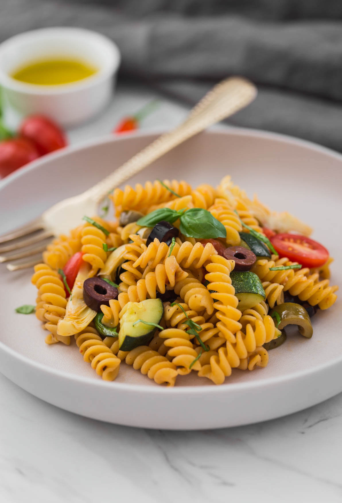 Pasta with artichoke and olives on a serving plate with a spoon.