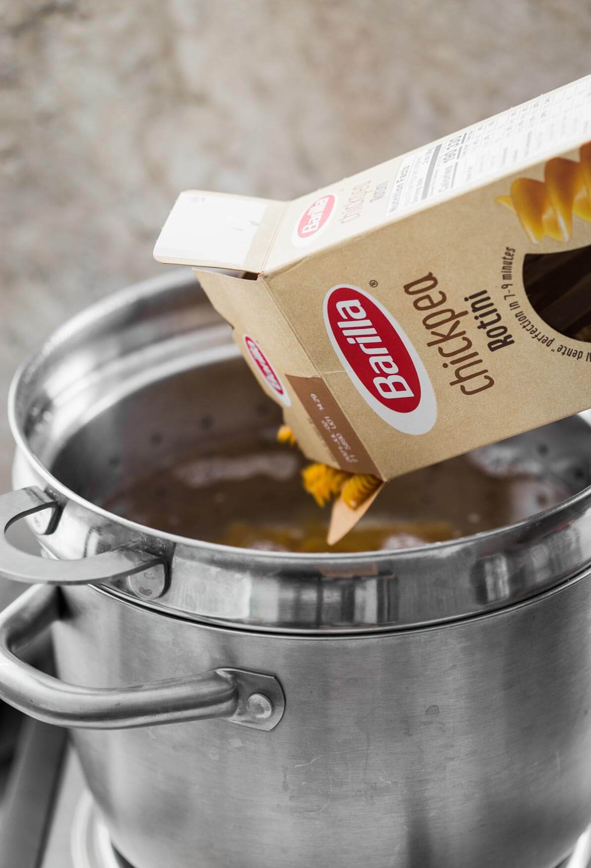 Rotini pasta while pouring in a large stainless steel pot.