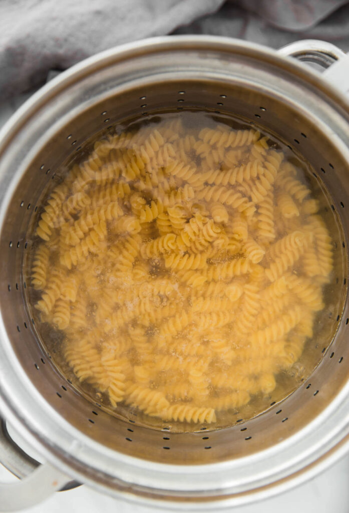 rotini in boiling water in a large stainless steel pot.