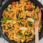Healthy Mediterranean pasta with artichokes and olives in a large skillet with a wooden spatula.