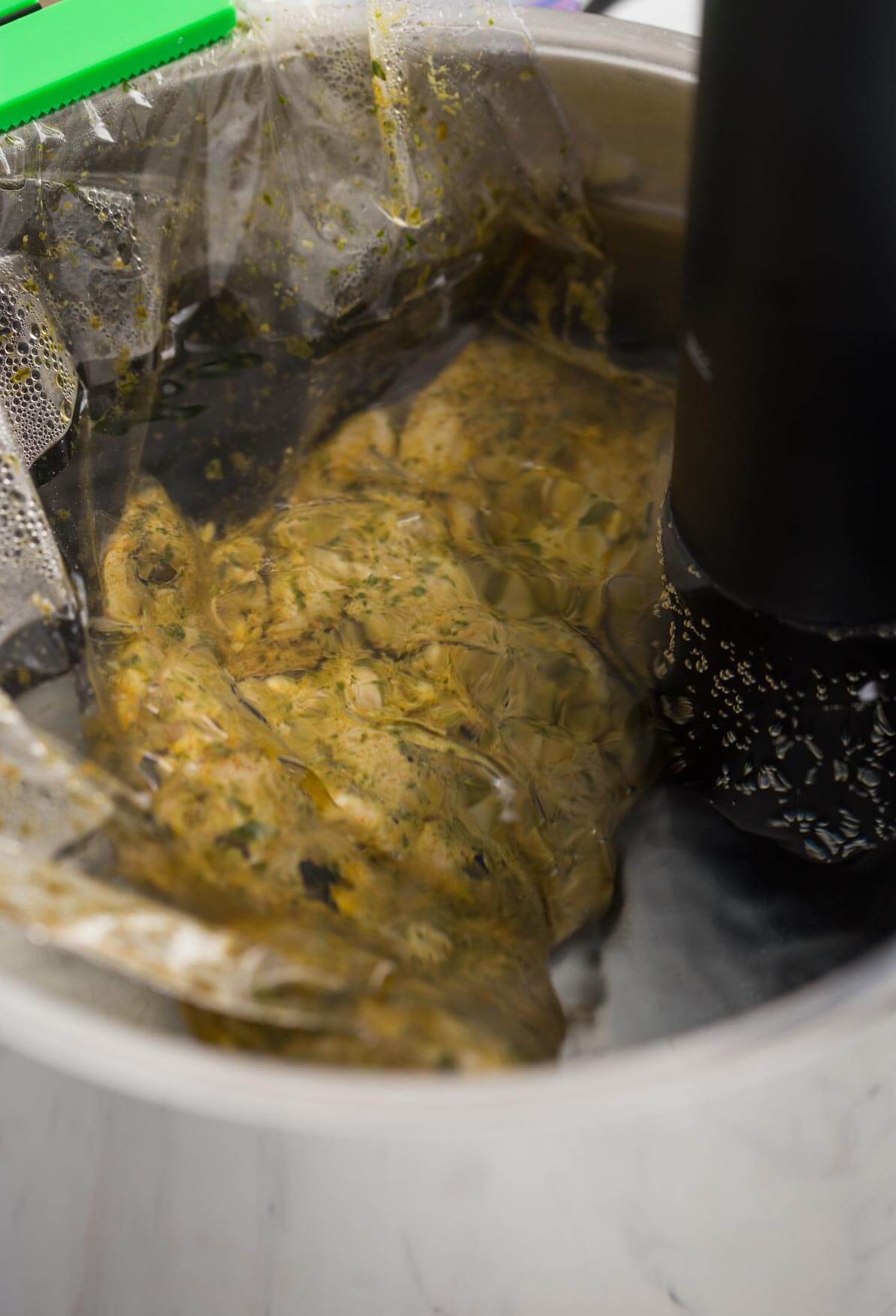 Image of vacuum-sealed chicken thighs in the cilantro-lime marinade while cooking in sous vide water bath.