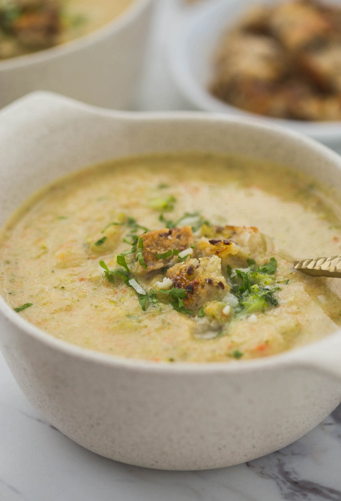 blended detox broccoli soup topped with croutons and fresh herbs in a soup bowl with a spoon