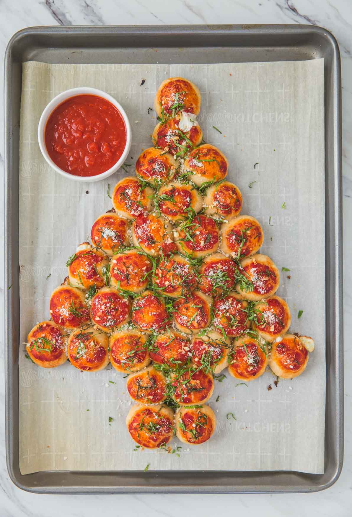 ready to serve pull apart Christmas tree pizza bites on a baking sheet and pizza sauce on the side for dipping.