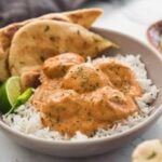 Butter chicken meatballs in a serving dish with naan bread, plain rice, lime wedge and green chili on the side.