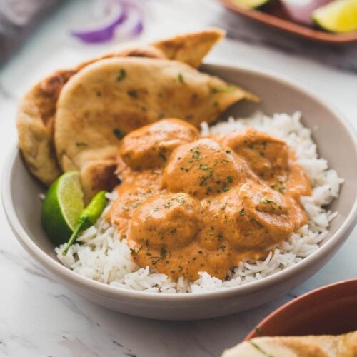 Butter chicken meatballs in a serving dish with naan bread, plain rice, lime wedge and green chili on the side.