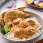 Butter chicken meatballs in a serving dish with naan bread, plain rice, lime wedge and green chili on the side.