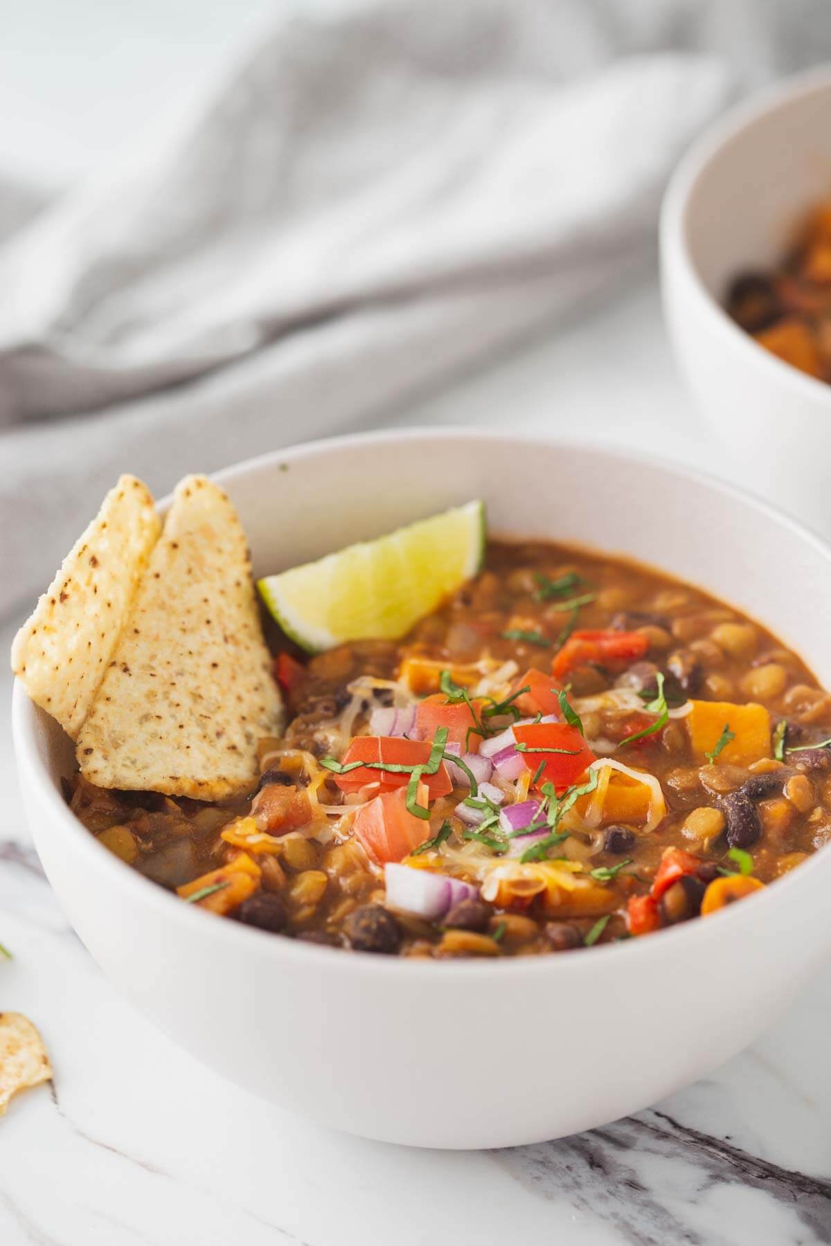 Sweet potato lentil chili in a serving soup bowl. Garnished with tortilla chips and lime wedges.