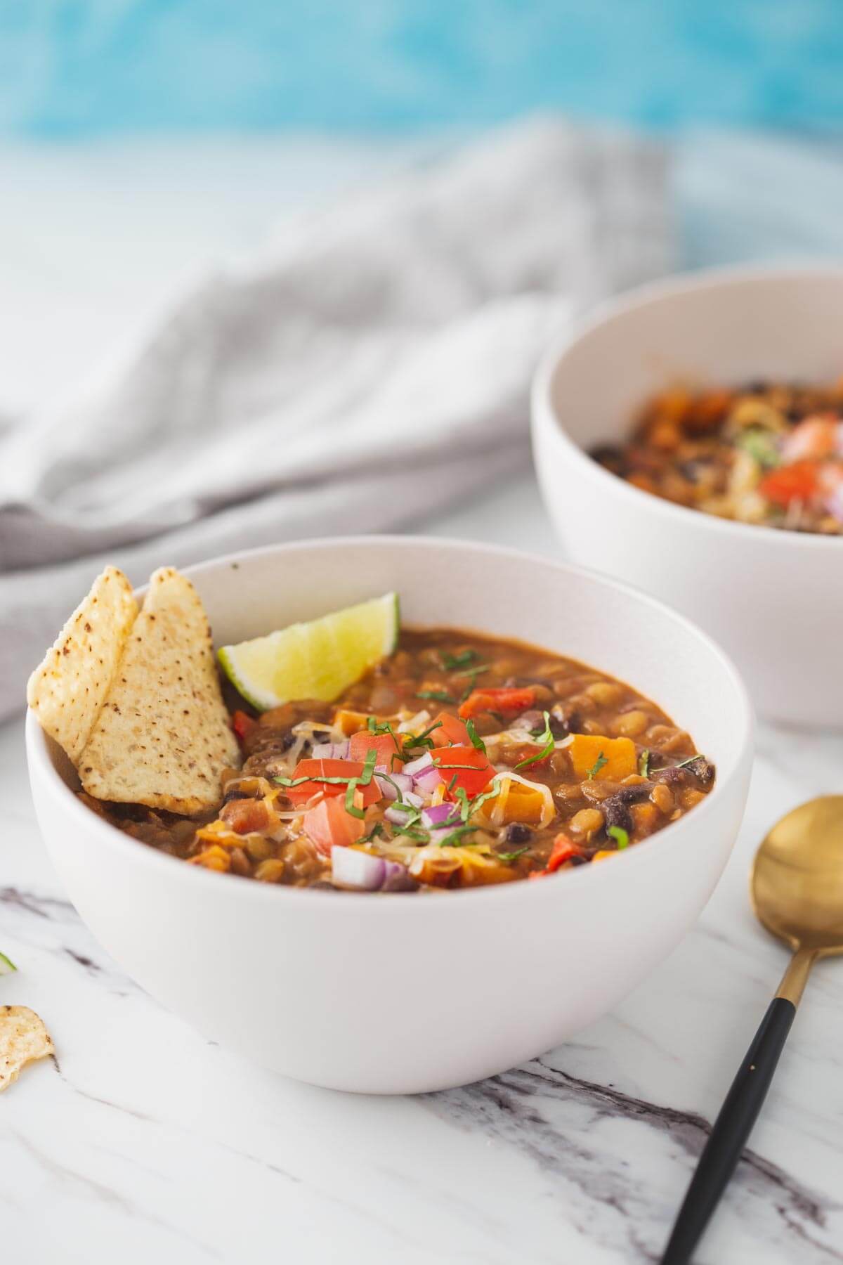 Sweet potato lentil chili in a serving soup bowl. Garnished with tortilla chips and lime wedges.