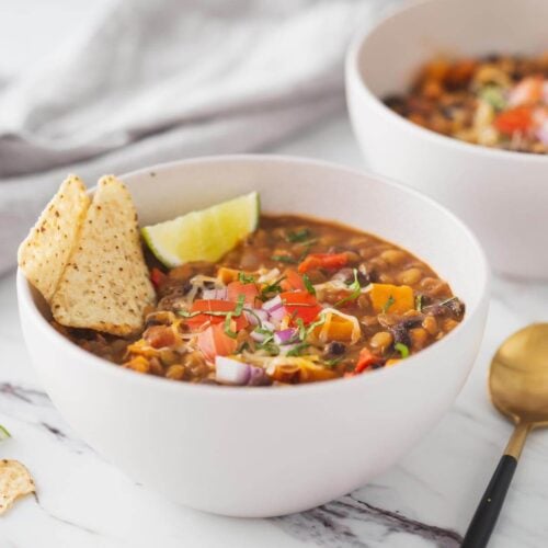 Sweet potato lentil chili in a serving soup bowl. Garnished with tortilla chips and lime wedges.