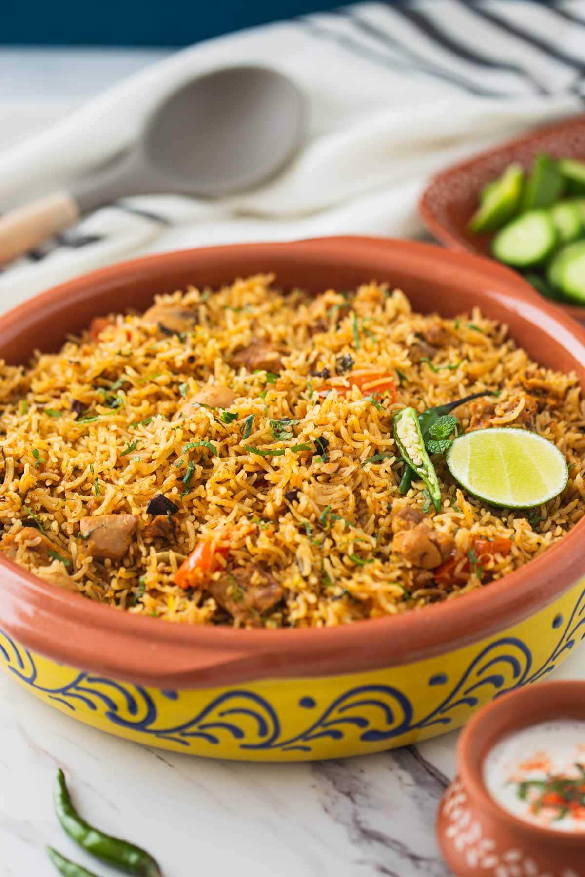 Authentic chicken biryani in a serving dish. Garnished with fresh green chili and a lemon slice.
