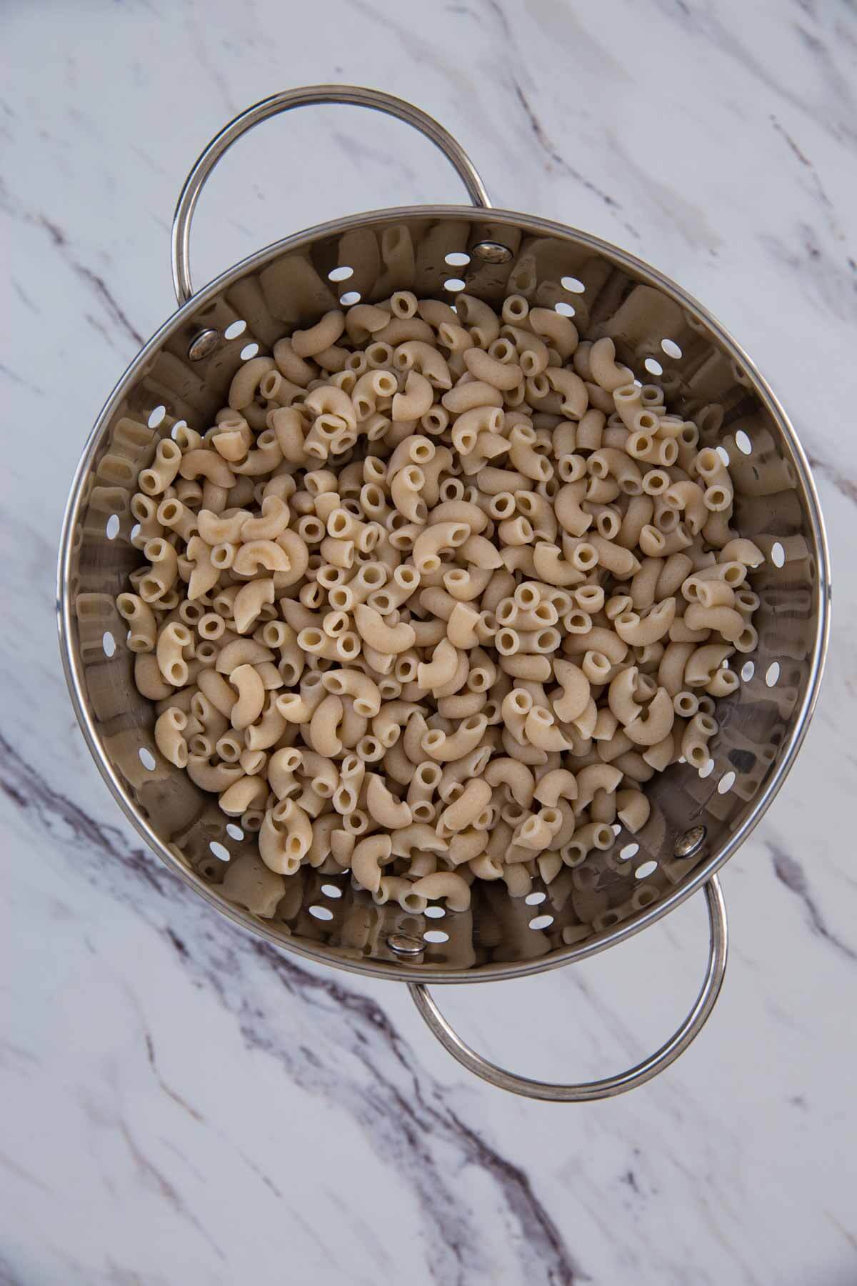 cooked pasta in a stainless steel colander read to prepare kale pasta dish.