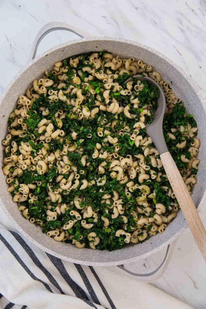 pesto kale pasta in a large frying pan with serving spoon.