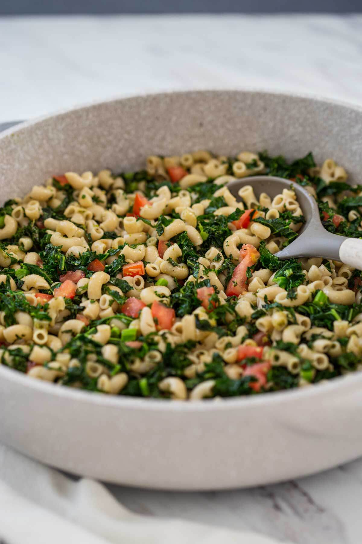 pesto kale pasta in a large frying pan with serving spoon.