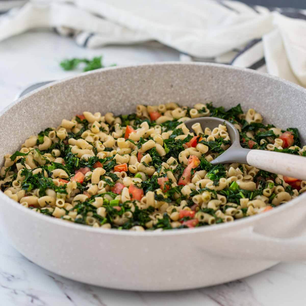 pesto kale pasta in a large frying pan with serving spoon.