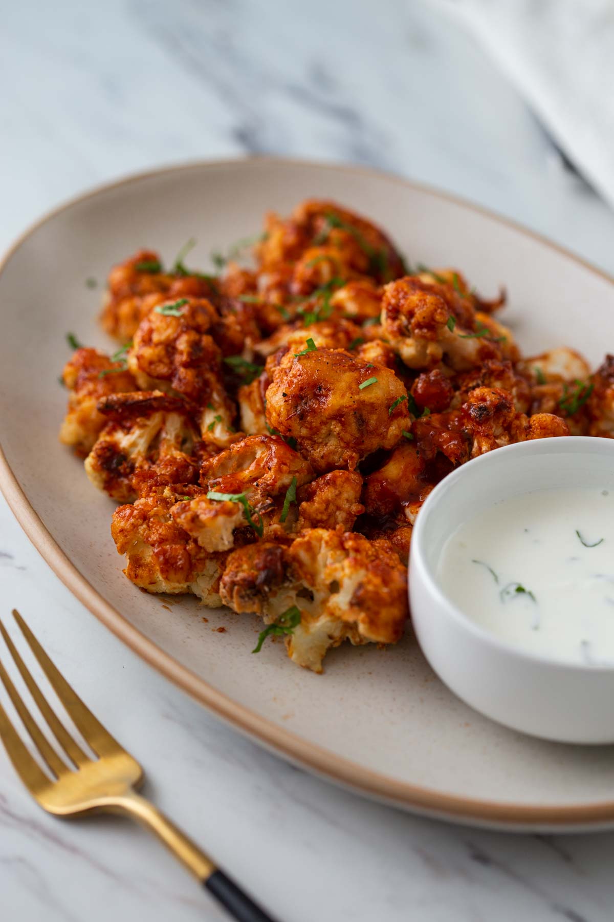 Air fryer bbq cauliflower bites in a serving dish with dipping sauce on the side.