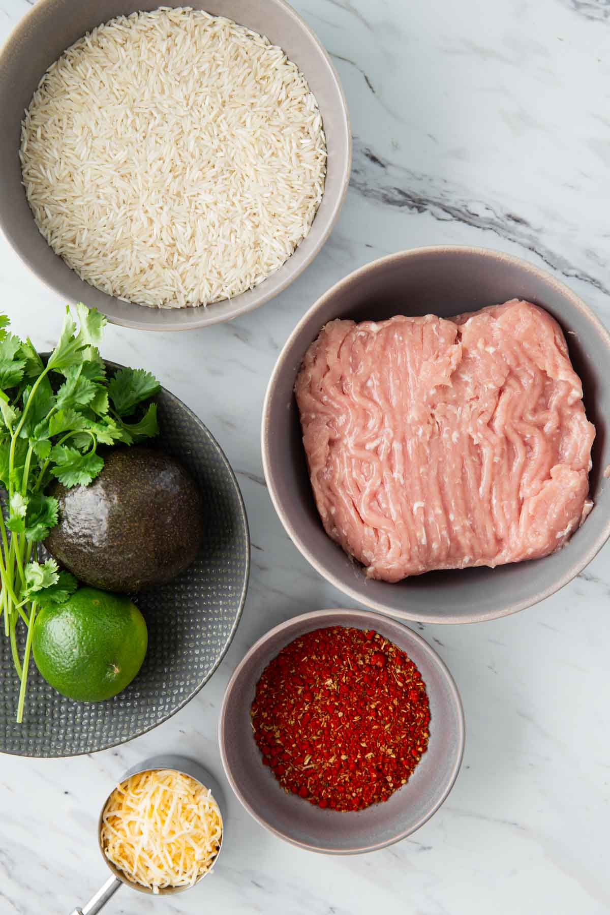 image with raw rice, ground chicken, taco seasoning mix, cheese and avocado gathered for making healthy taco rice.