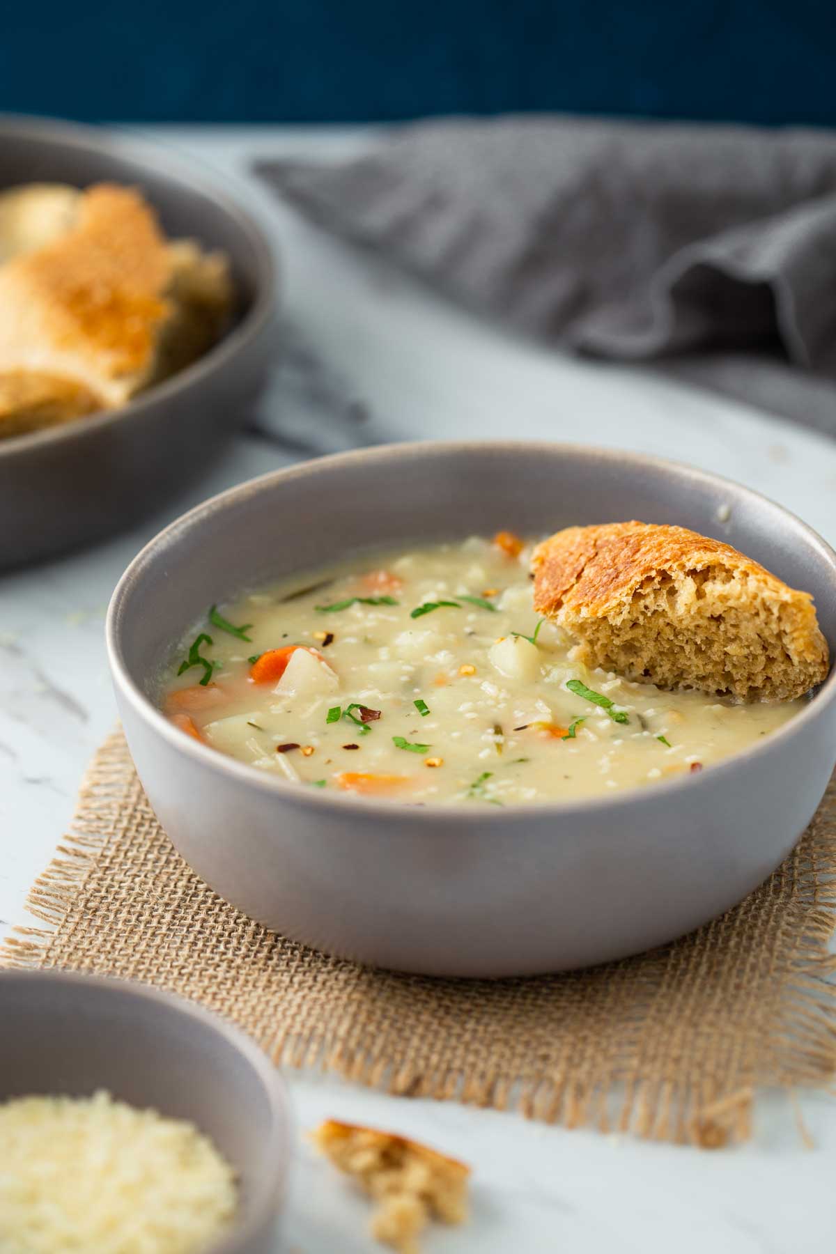 Creamy potato soup with a piece of bread in a serving bowl. There is plate full of bread and napkin in the background.