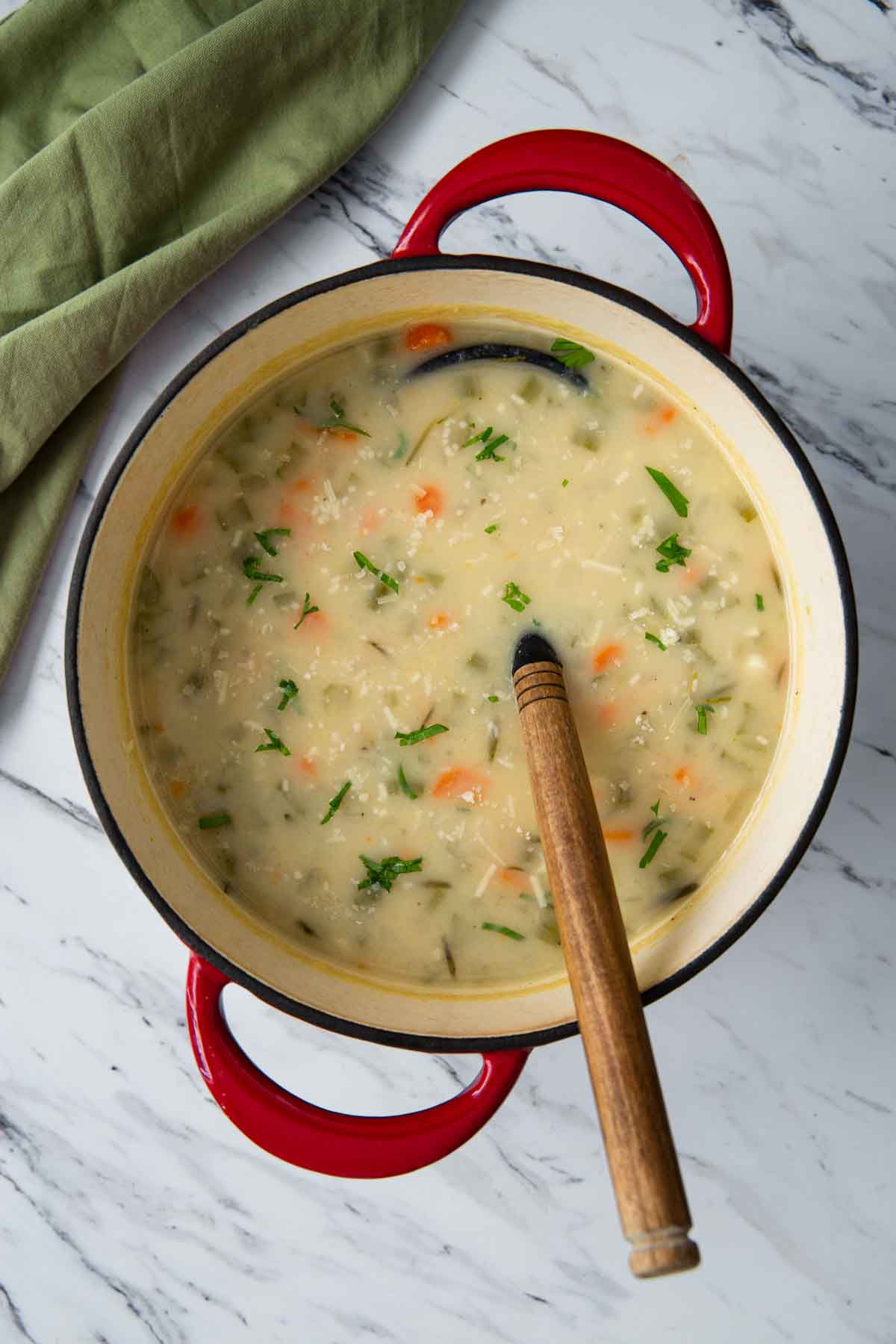 One pot creamy potato soup garnished with fresh parsley in a dutch oven with a wooden ladle. 