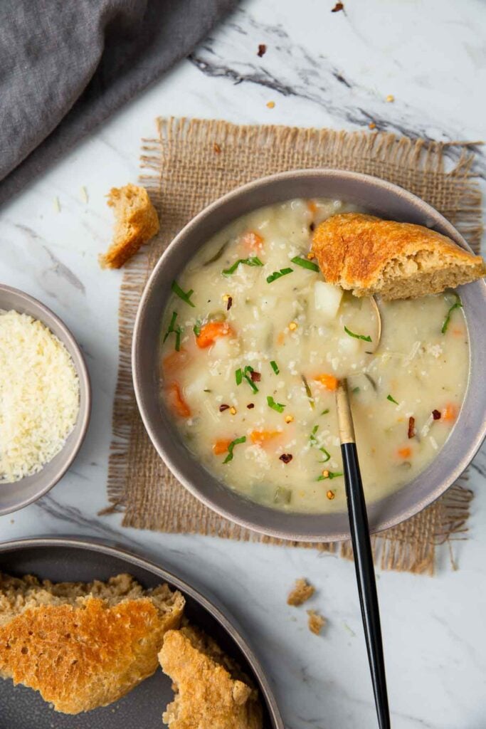 Creamy healthy potato soup with a piece of bread and a metal spoon in a serving bowl. 