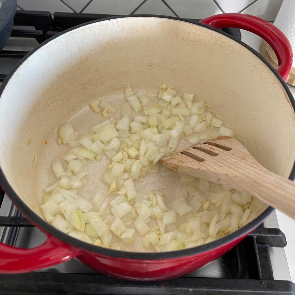 Sautéing onion and garlic in a dutch oven with a wooden spatula on gas stove.  